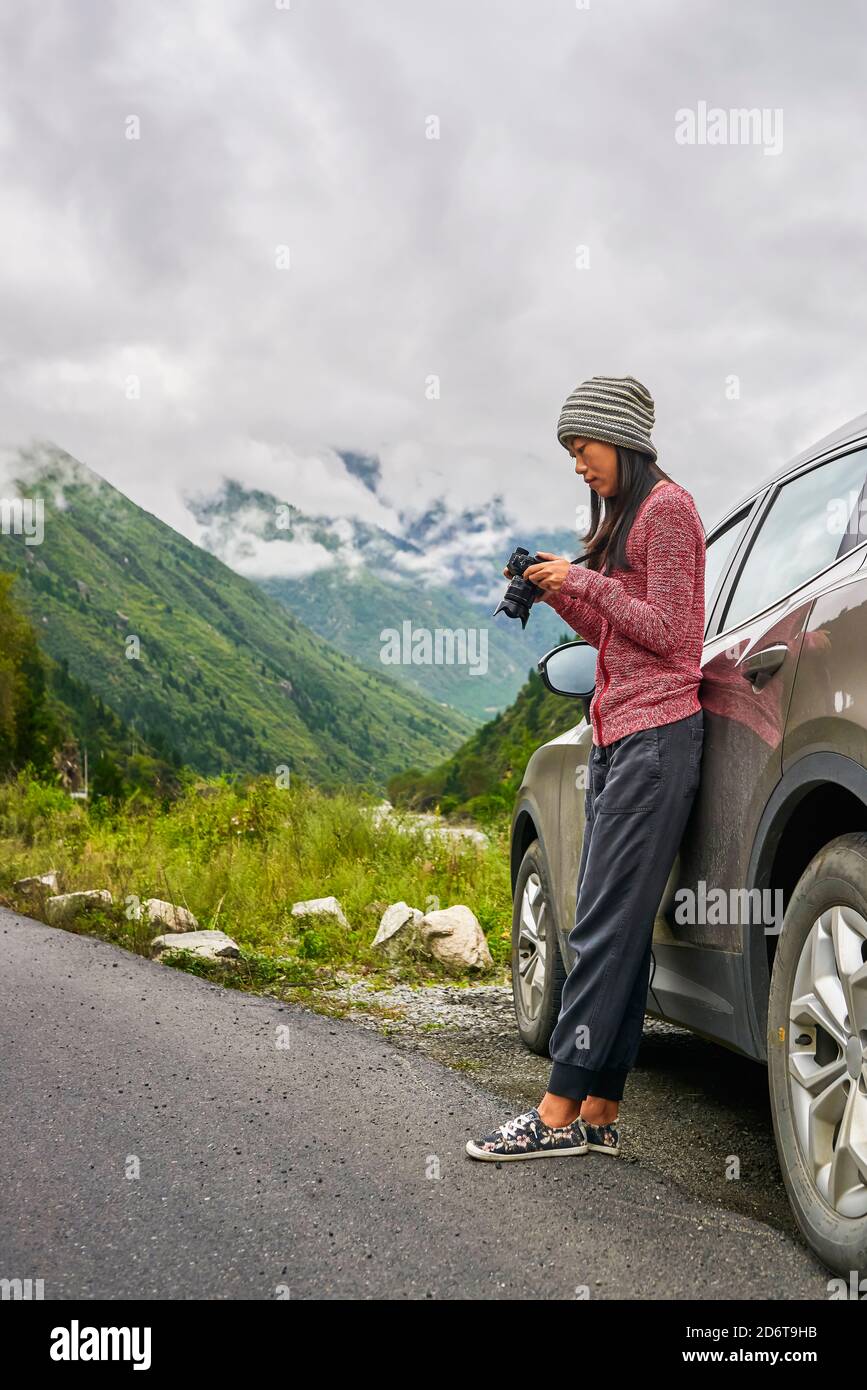 Seitenansicht der jungen nachdenklichen asiatischen Frau in Sportswear ruhen Auf dem Auto mit Fotokamera im grün bewölkten Tal Stockfoto