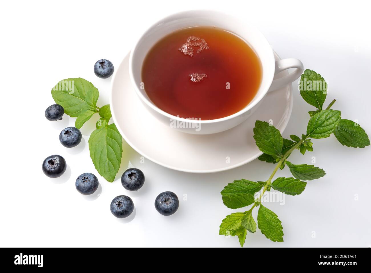 Eine Tasse schwarzen Tee auf einer Untertasse mit Minzblättern und Heidelbeeren auf einem weißen isolierten Hintergrund. Stockfoto