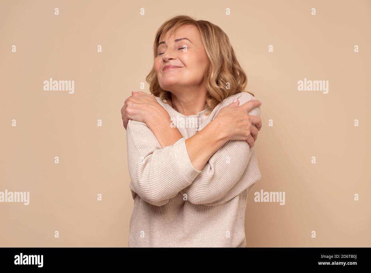 Ältere kaukasische Frau umarmt sich glücklich und positiv, lächelnd zuversichtlich Stockfoto