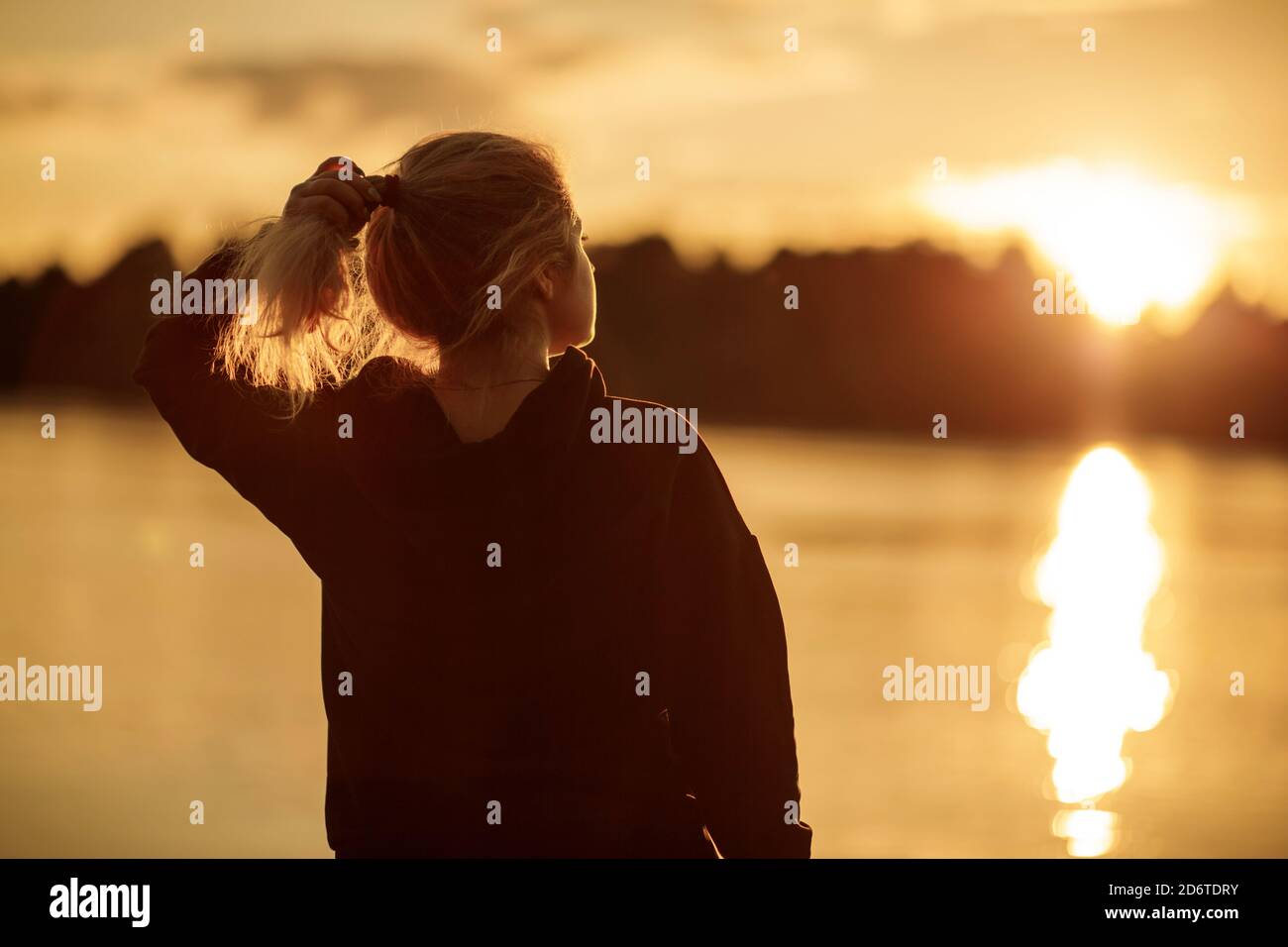 Eine junge Frau schaut auf die untergehende Sonne in der Nähe des Flusses. Stockfoto