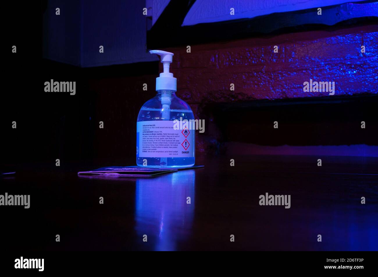 Handdesinfektionsflasche auf einem Tisch in einem Pub mit violetter/blauer Beleuchtung Stockfoto
