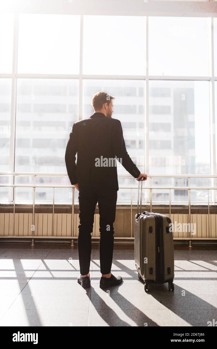 Mann, der mit einem Koffer neben dem riesigen Fenster steht Stockfoto