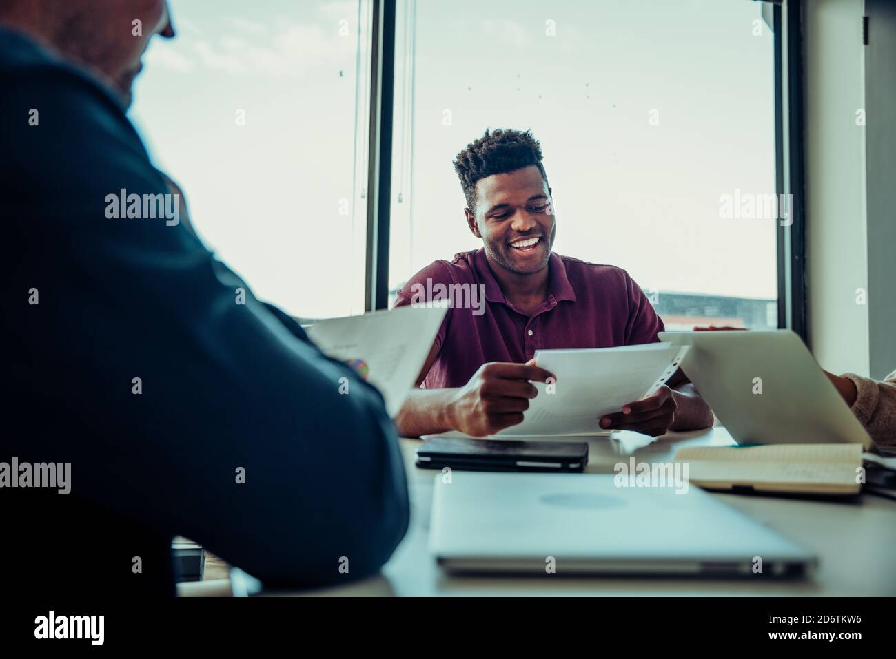 Männlicher Geschäftsmann, der lachend mit Kollegen über Punkte diskutiert Zur Verbesserung der Geschäftsabläufe Stockfoto