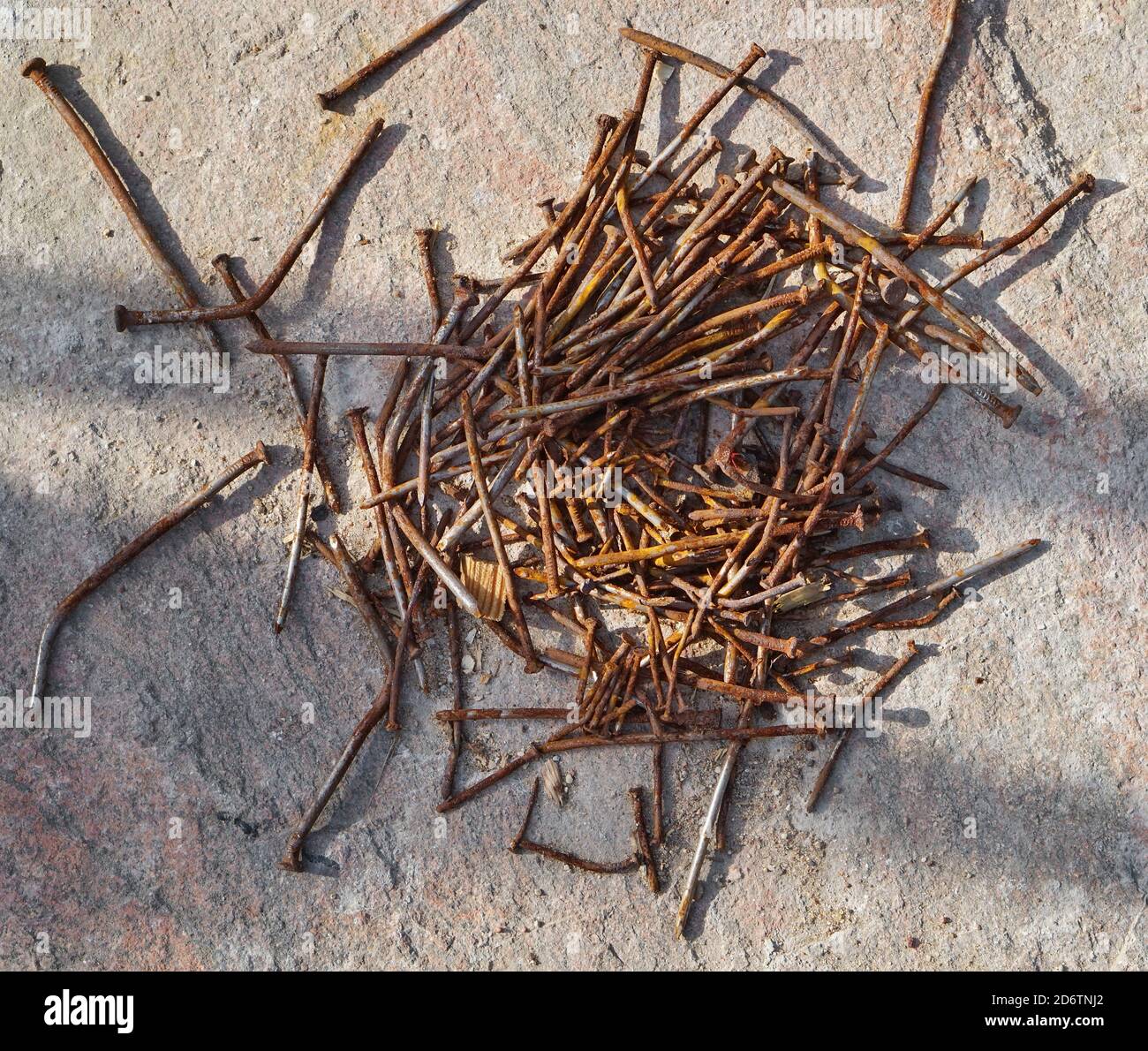 Haufen von rostigen gebogenen Nägeln sind auf Granitstein gestapelt. Stockfoto