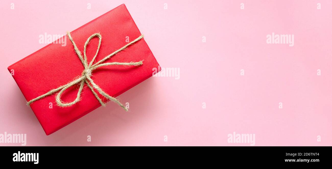 Rote Geschenkbox mit Garn auf einem hellrosa Hintergrund gebunden. Banner. Urlaubskonzept. Weihnachten, Muttertag, Valentinstag, Internationaler Frauentag Stockfoto