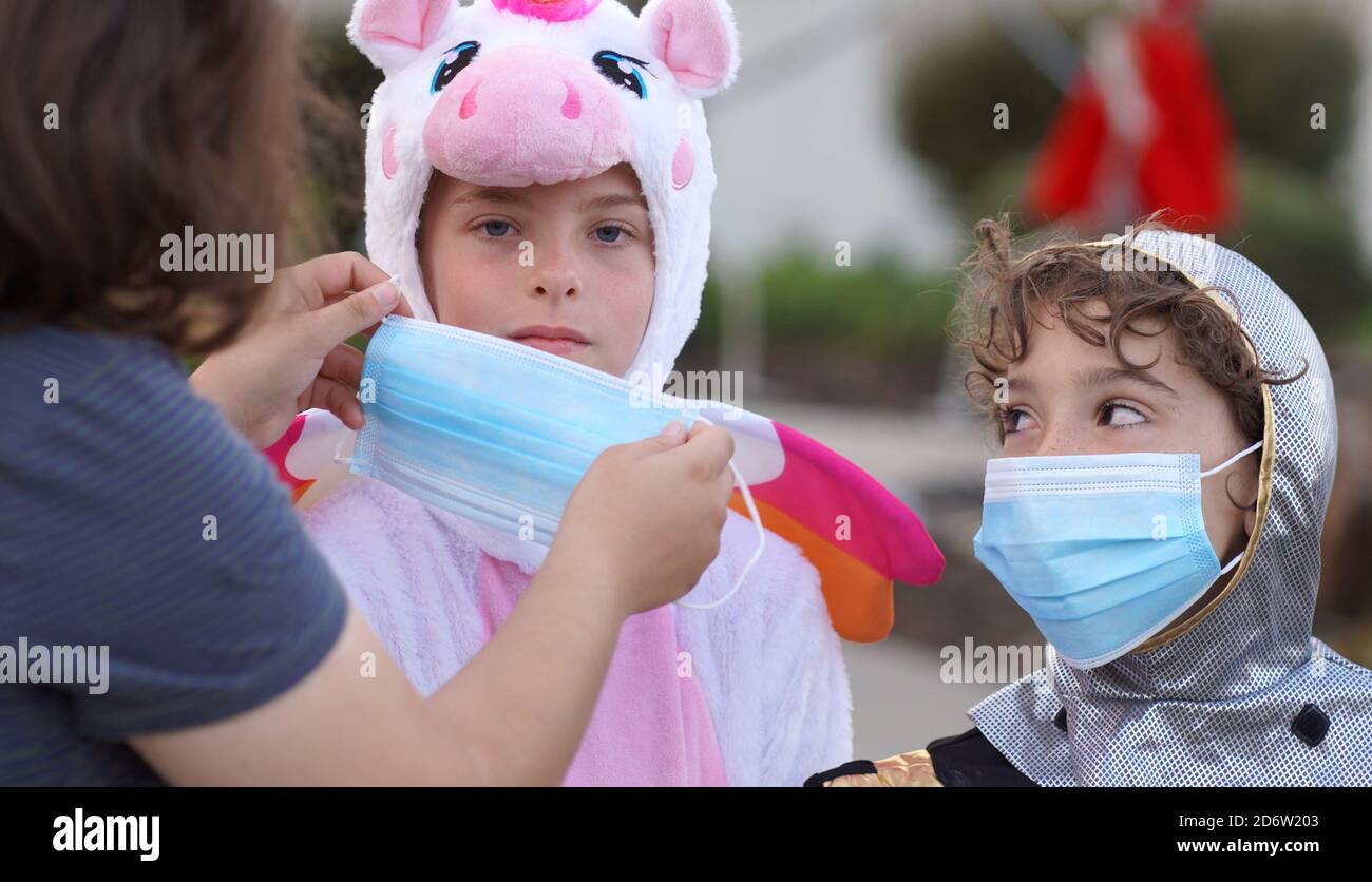 Eine Mutter legt ihren beiden Kindern Gesichtsmasken an An Halloween sicher bleiben Stockfoto