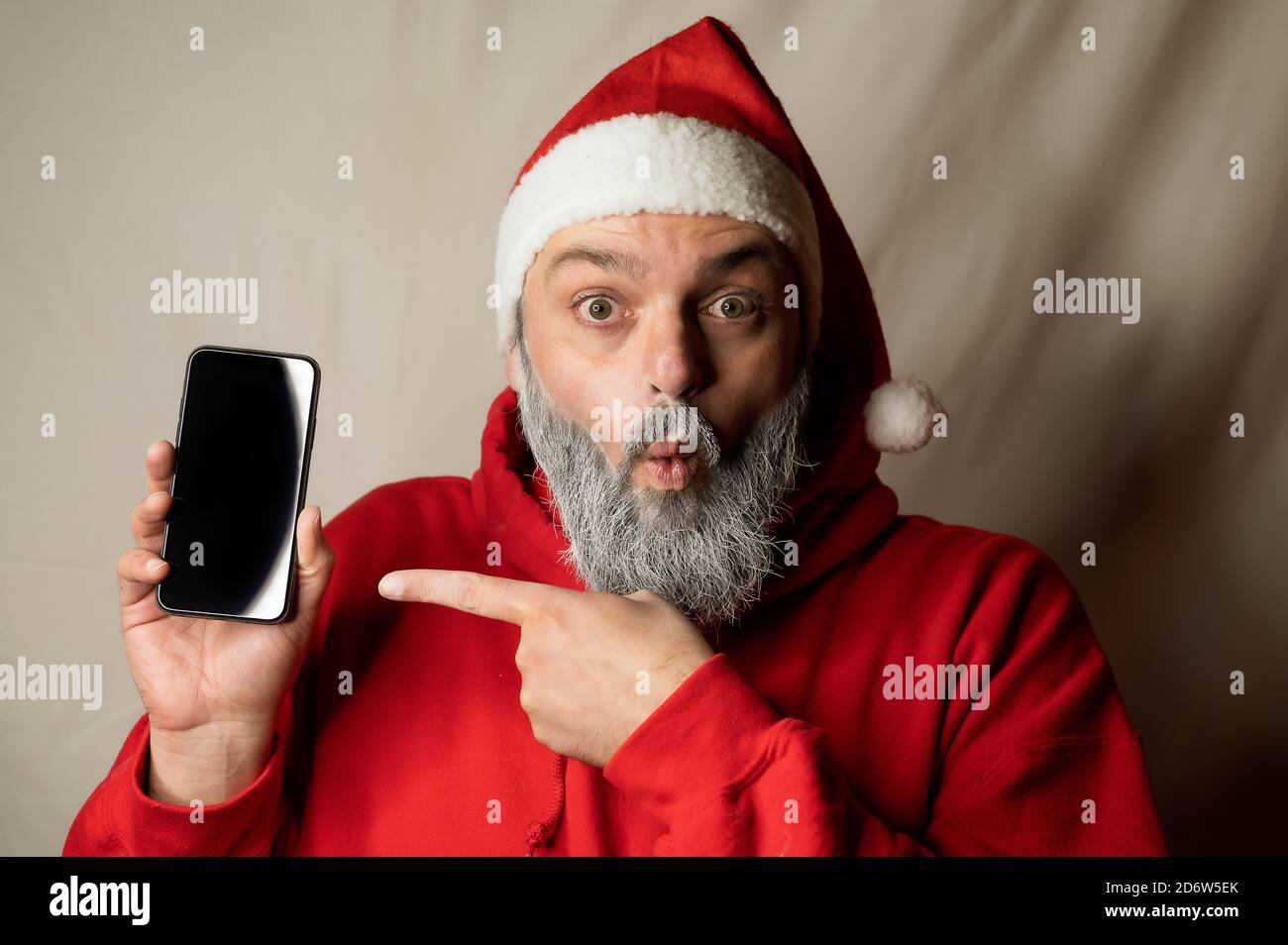 der weihnachtsmann zeigt überrascht auf sein Handy Stockfoto