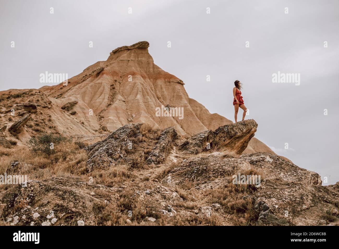Frau auf einem roten Kleid auf einem Felsen in einer desertischen Landschaft in der Barcenas Reales Wüste in Navarra, Spanien Stockfoto