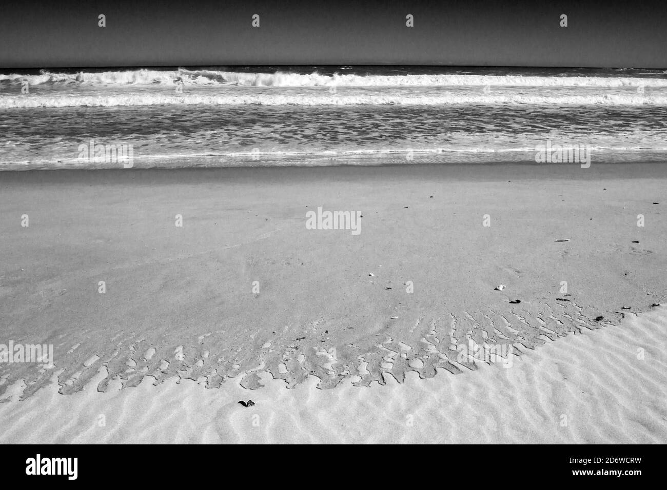 Muster, die an einem Sandstrand zurückgelassen wurden, nachdem sich eine Welle in Monochrome zurückgezogen hatte, fotografiert an der Westküste Südafrikas Stockfoto