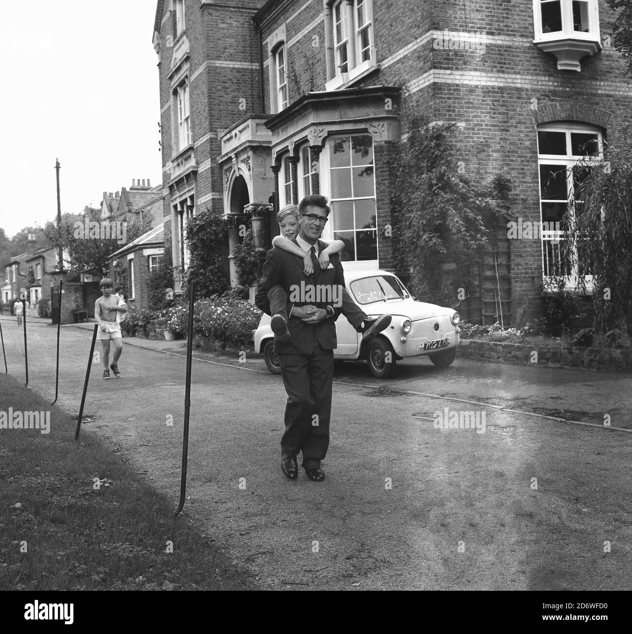 1970, historisch, ein Schulmeister eines Jungen nur staatlichen Internat, die einen Huckepack Lift zu einem müden Schuljungen nach einer anstrengenden PE-Lektion, Lewisham, South East London, England, Großbritannien. Lehrer zu sein beinhaltet viele verschiedene Dinge! Das Wort Huckepack ist vermutlich aus dem 16. Jahrhundert "Pick Pack", eine Last, die auf den Rücken einer Person zum Tragen aufgeschlagen wurde kommen. Stockfoto