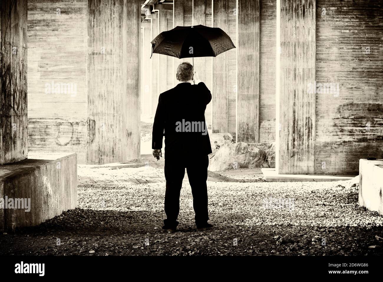 Künstlerisches kreatives Bild eines unverkennbaren Mannes im Anzug, der einen Regenschirm in einer konkreten Umgebung hält. Stockfoto