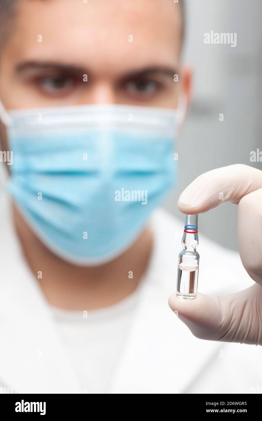 Nahaufnahme des Arztes mit OP-Maske hält eine Ampulle mit Impfstoff in der Hand - konzentrieren Sie sich auf die Ampulle Stockfoto