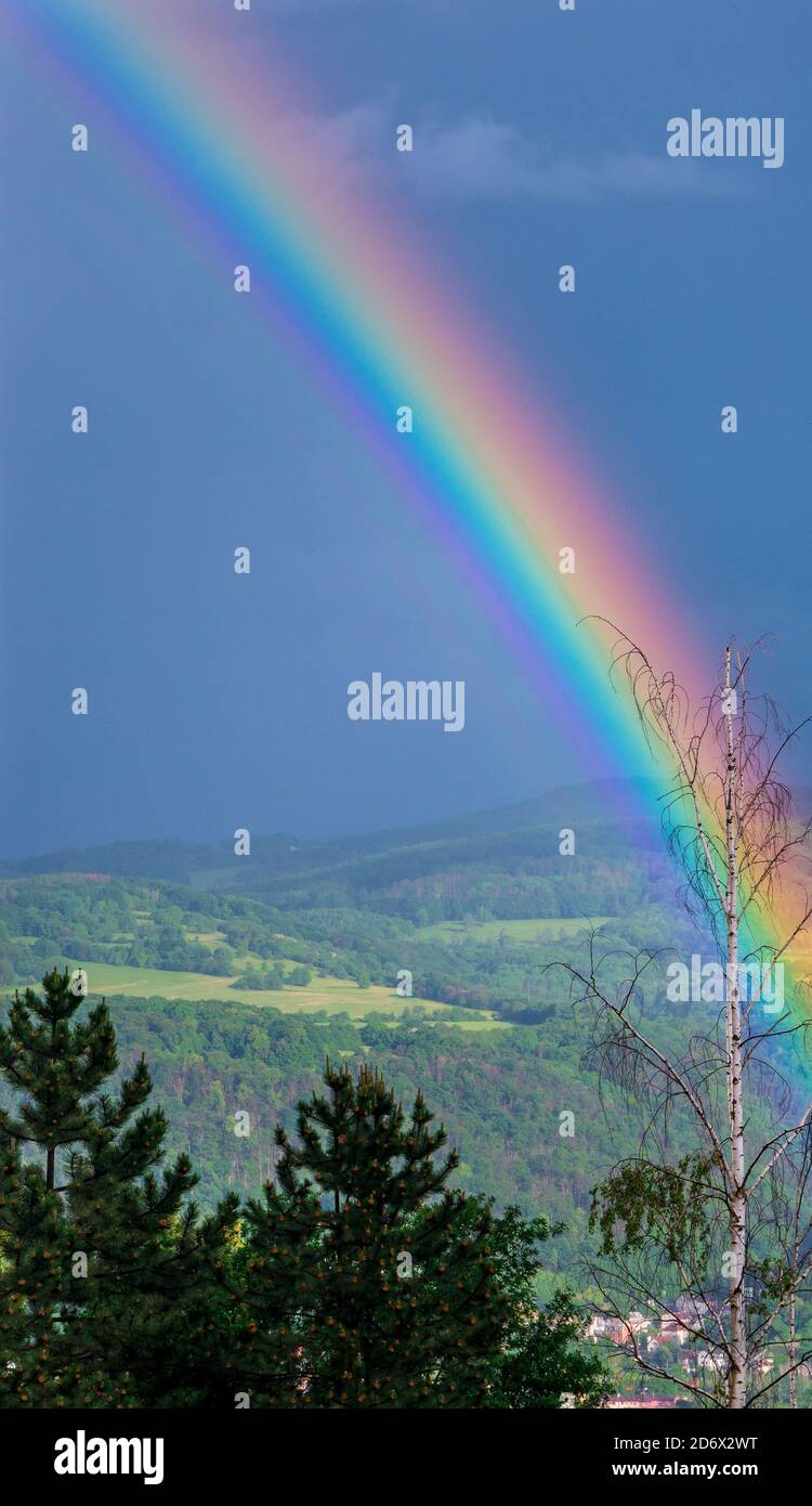 Schöner intensiver Regenbogen steigt aus dem Tal. Erscheint ein paar Augenblicke nach heftigem Regen, der eine helle Sonne erzeugt. Stockfoto