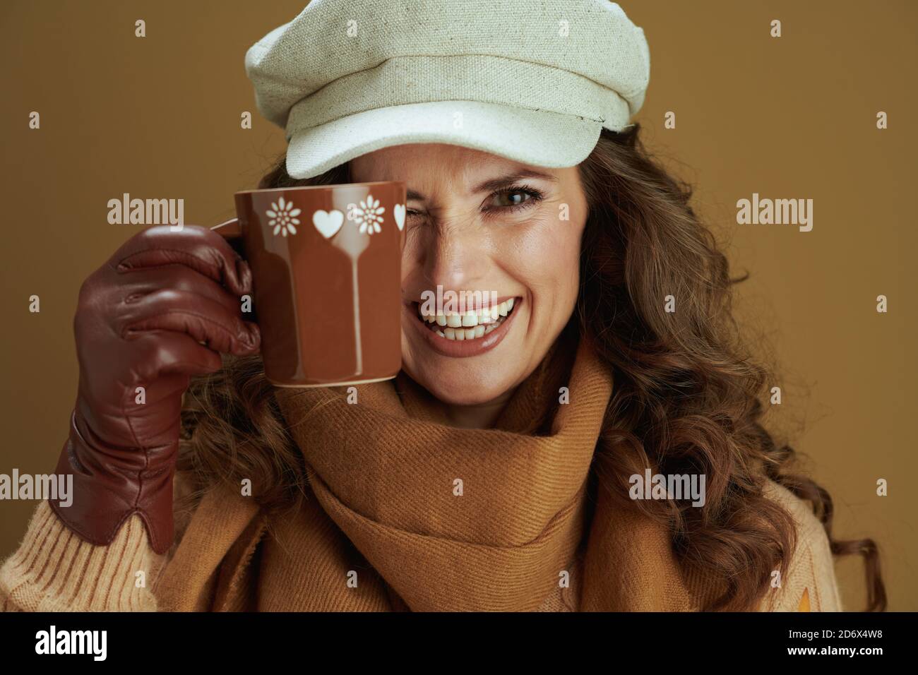 Hallo oktober. Portrait der lächelnden trendigen Hausfrau in Schal mit Lederhandschuhen und Tasse isoliert auf beigem Hintergrund. Stockfoto