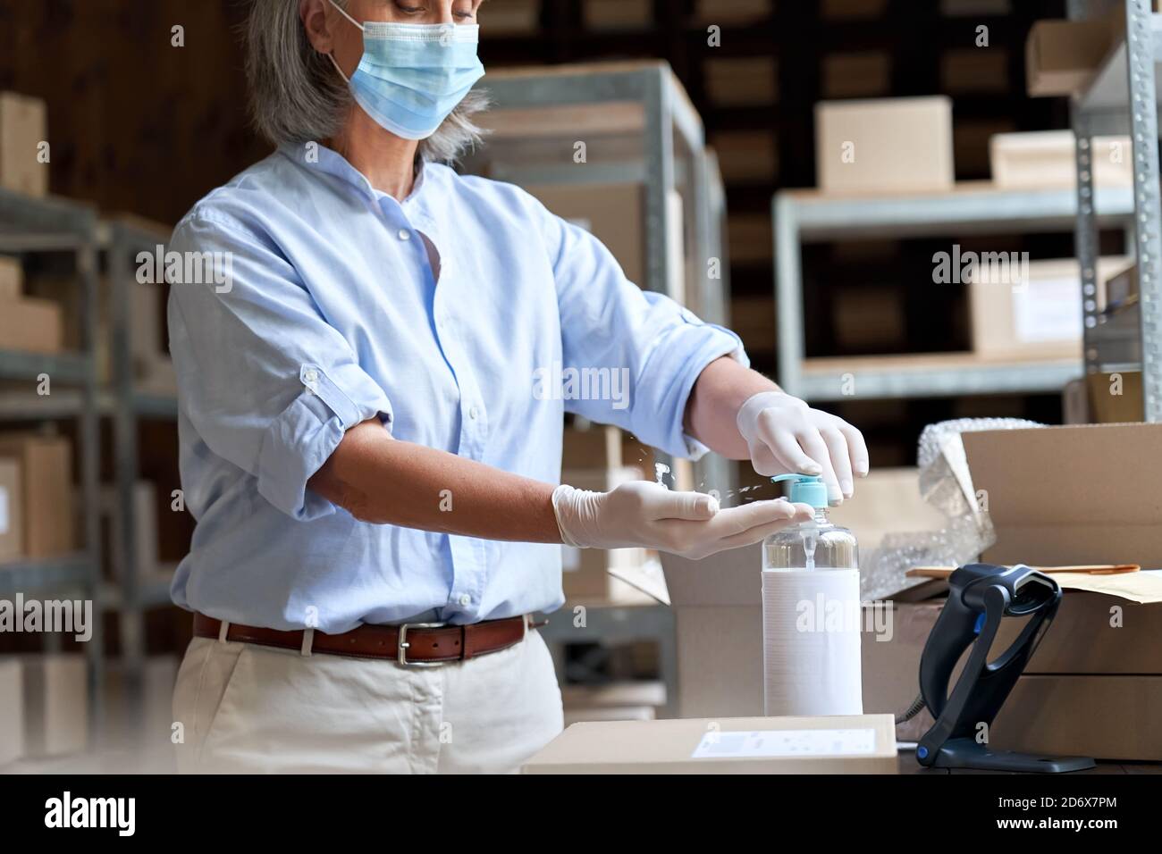 Reife weibliche Lagerarbeiterin trägt Maske mit Desinfektionsmittel bei der Arbeit. Stockfoto