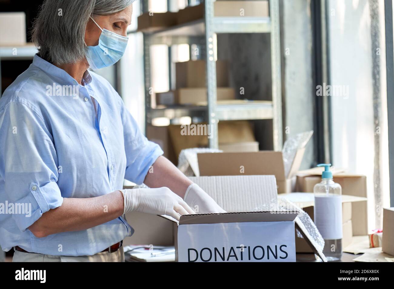 Reife Frau Lagerarbeiter trägt Maske Verpackung Spenden Box. Stockfoto