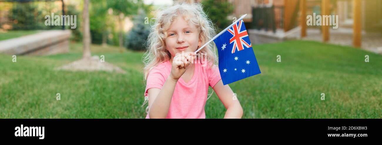 Glückliches kaukasisches Mädchen mit australischer Flagge. Lächelndes Kind, das auf Gras sitzt und die australische Flagge hält. Kinderbürger feiert Australien Tag Urlaub in Stockfoto