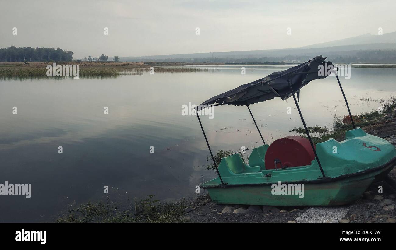 Foto eines leeren Bootes, das am Seeufer gestrandet ist Berge im Hintergrund Stockfoto
