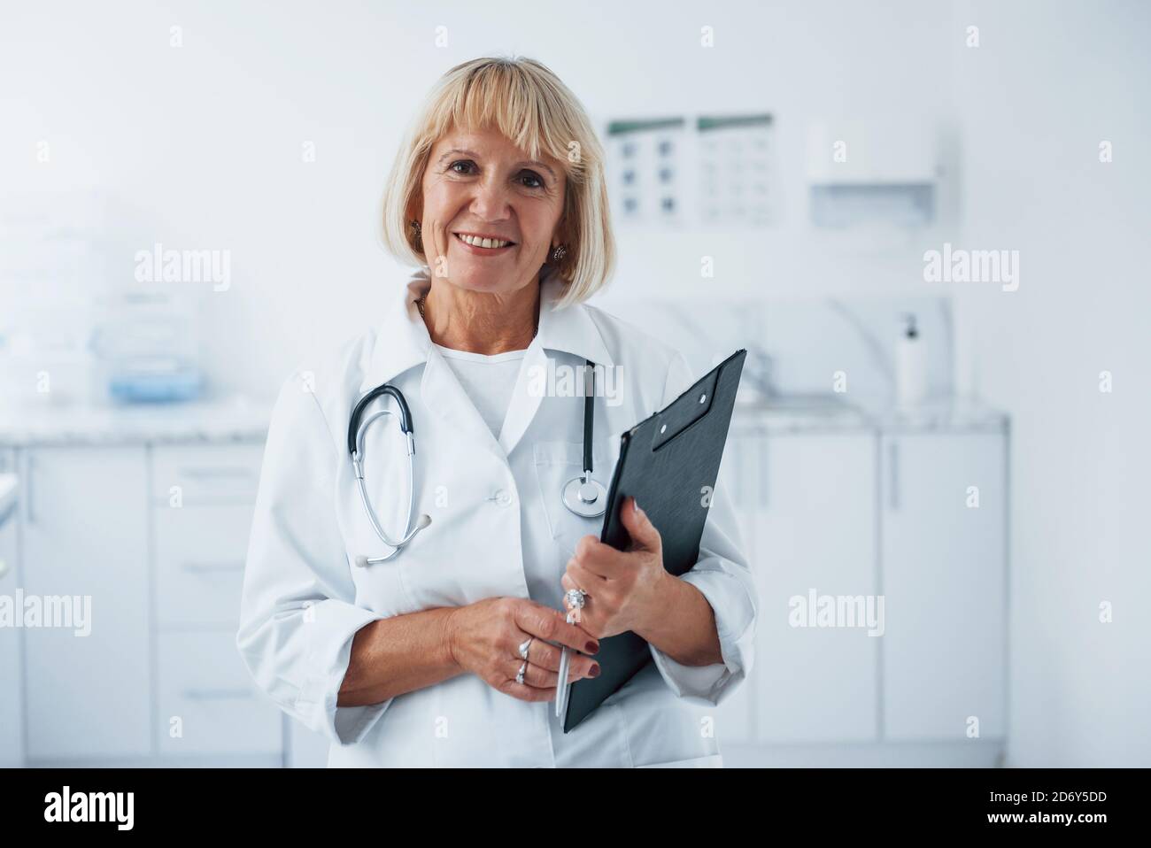 Mit Notizblock in den Händen. Porträt des Oberarztes in weißer Uniform, die in der Klinik steht Stockfoto