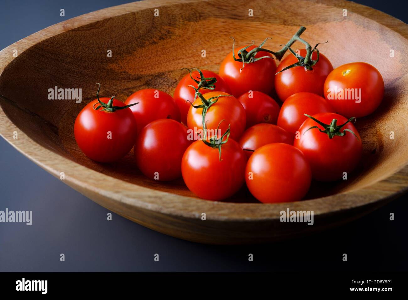 Frische, reife, kleine rote Tomaten, Solanum lycopersicum, in einer Holzschüssel. Eine gesunde Quelle von Vitamin C, Kalium, Folat und Vitamin K Stockfoto