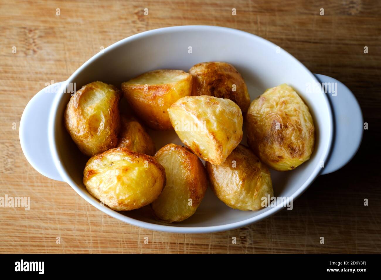 Eine kleine Schüssel mit heißen knusprigen Bratkartoffeln. Die Röster sind frisch aus dem Ofen, gut knusprig und eine leckere Ergänzung zu einem traditionellen Sonntagsbraten Stockfoto