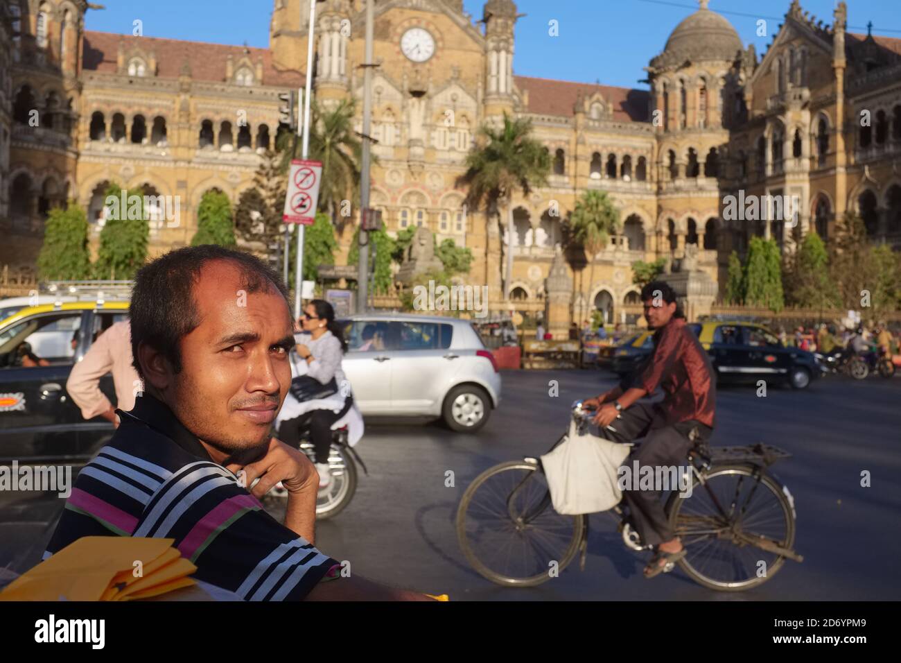 Ein Fußgänger, ein Radfahrer und motorisierter Verkehr vor dem berühmten Chhatrapati Shivaji Maharaj Terminus (CSMT), einem UNESCO-Weltkulturerbe in Mumbai, Indien Stockfoto