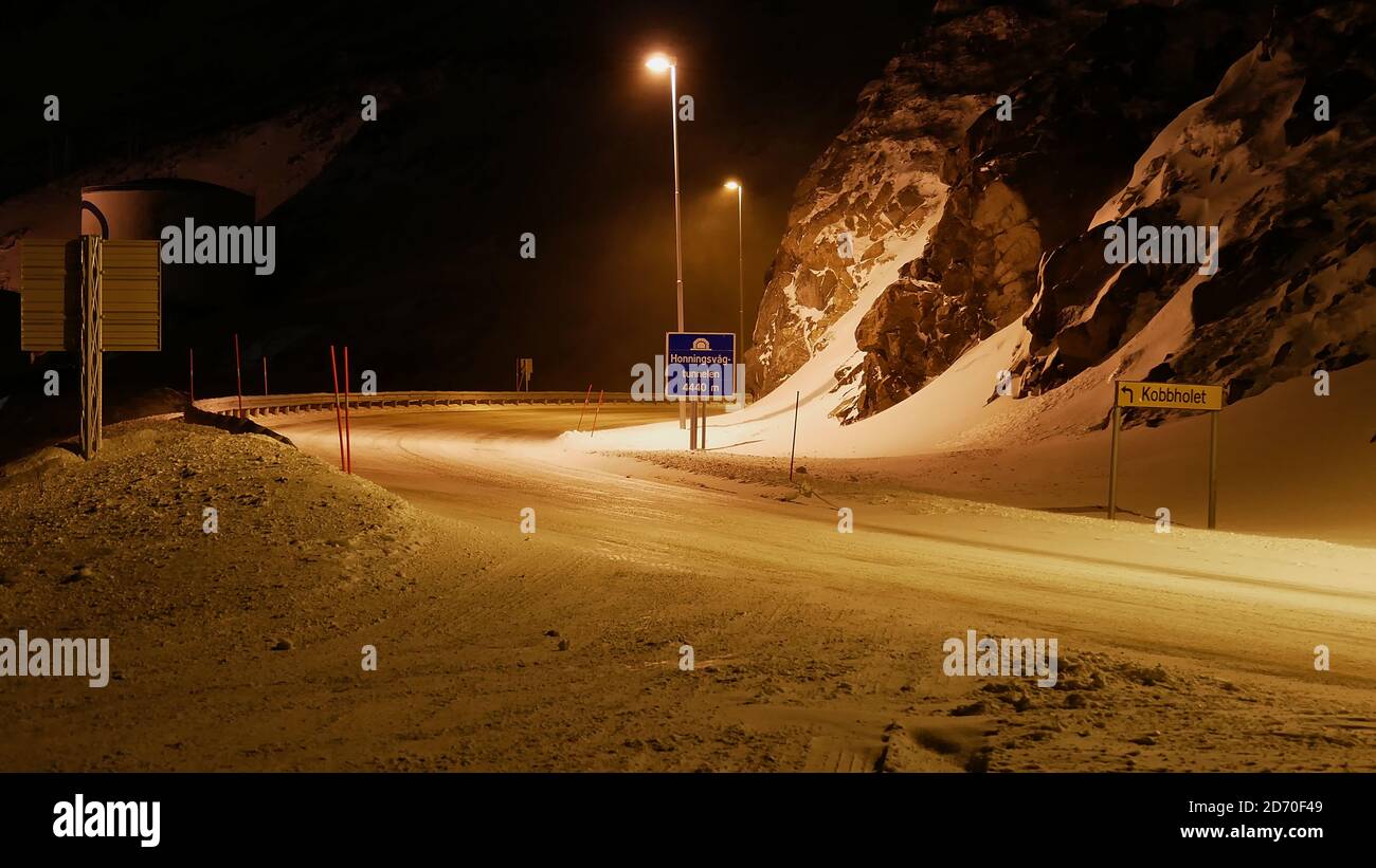 Eingang des Honningsvåg-Tunnels, der mit Nordkapp verbunden ist, mit Straßenschildern bei Nacht, Laternen und Schneepflug-Markierungen (Pfosten) bei widrigen Wetterbedingungen. Stockfoto
