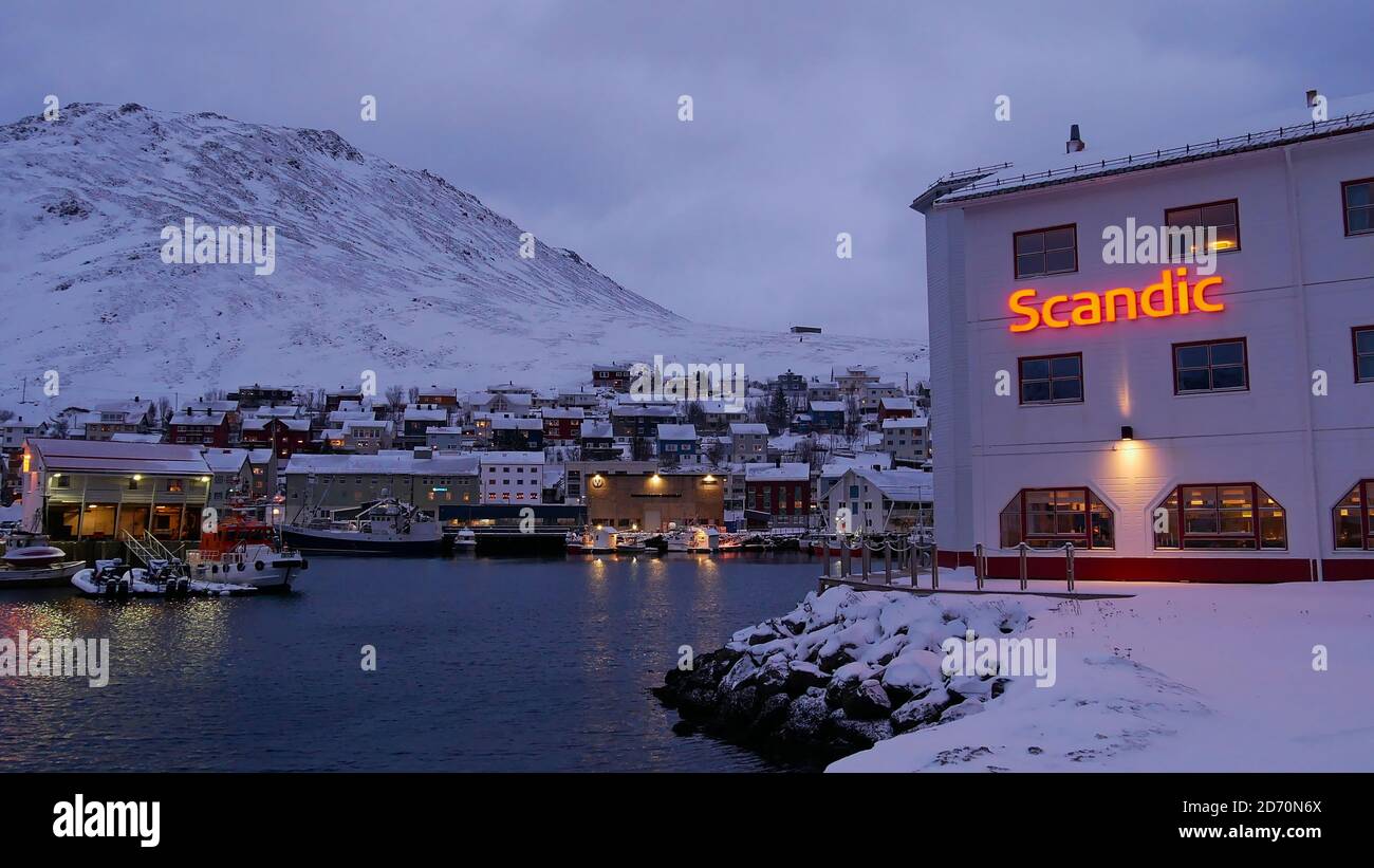 Honningsvåg, Norwegen - 02/27/2019: Hotel Scandic Bryggen mit beleuchtetem Logo am Hafen von Honningsvåg in der Nähe von Nordkapp mit Dorf und Schnee. Stockfoto