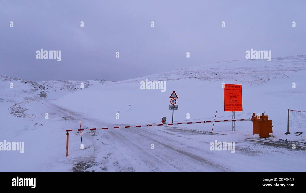 Skarsvåg, Norwegen - 02/28/2019: Geschlossenes Tor an der Straße zum beliebten Nordkapp (Nordkap) im Winter mit orangefarbenem Schild, das über die Konvoi-Stunden informiert. Stockfoto