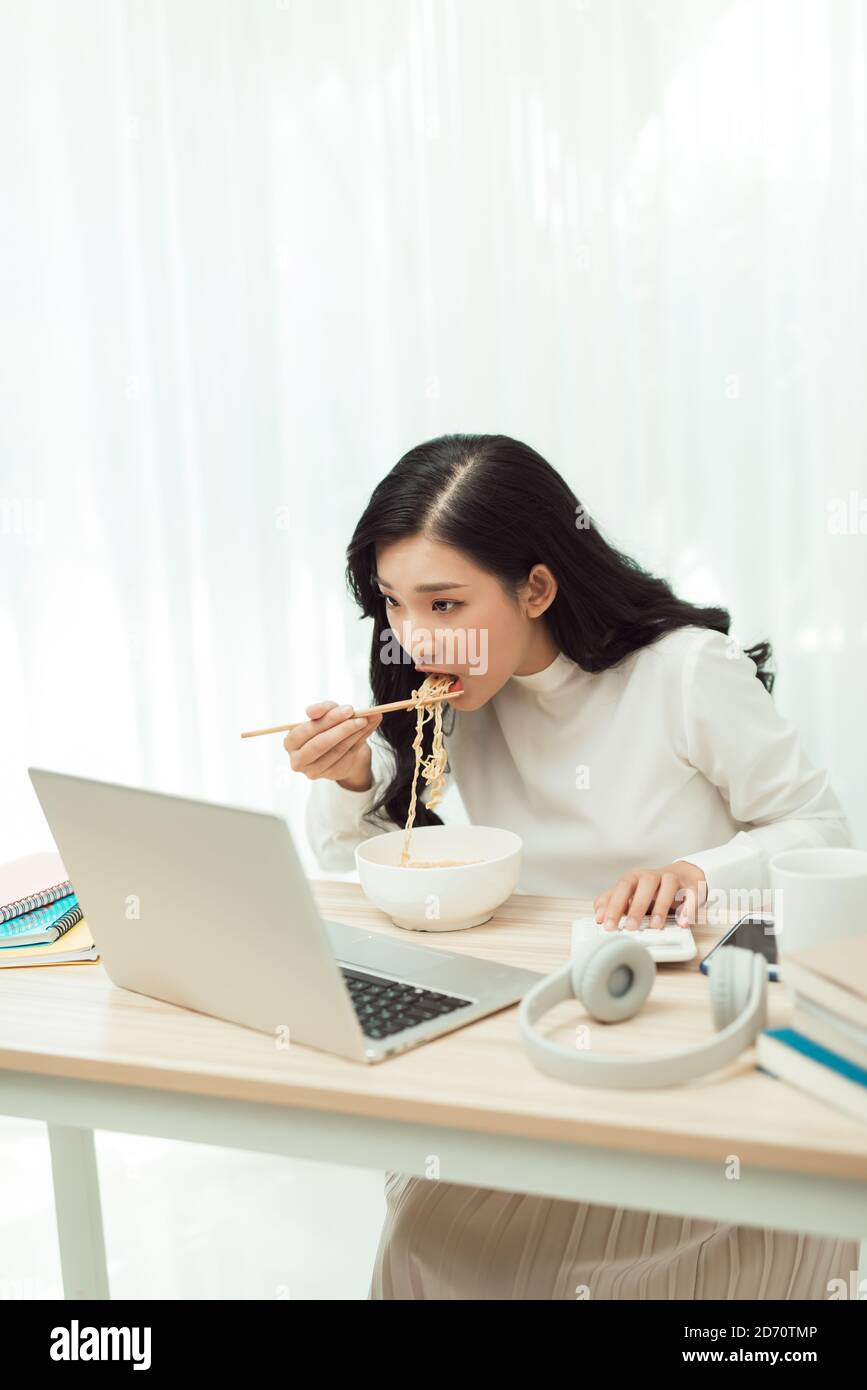Asien freiberufliche Geschäftsfrau essen Instant Nudeln während der Arbeit an Laptop im Wohnzimmer im Heimbüro Stockfoto