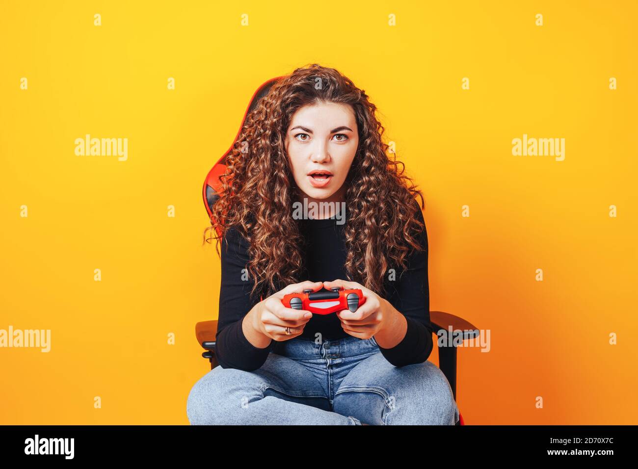 Frau, die hinter einem Spielstuhl in ihren Händen sitzt und rot hält Gamepad auf gelbem Hintergrund Stockfoto