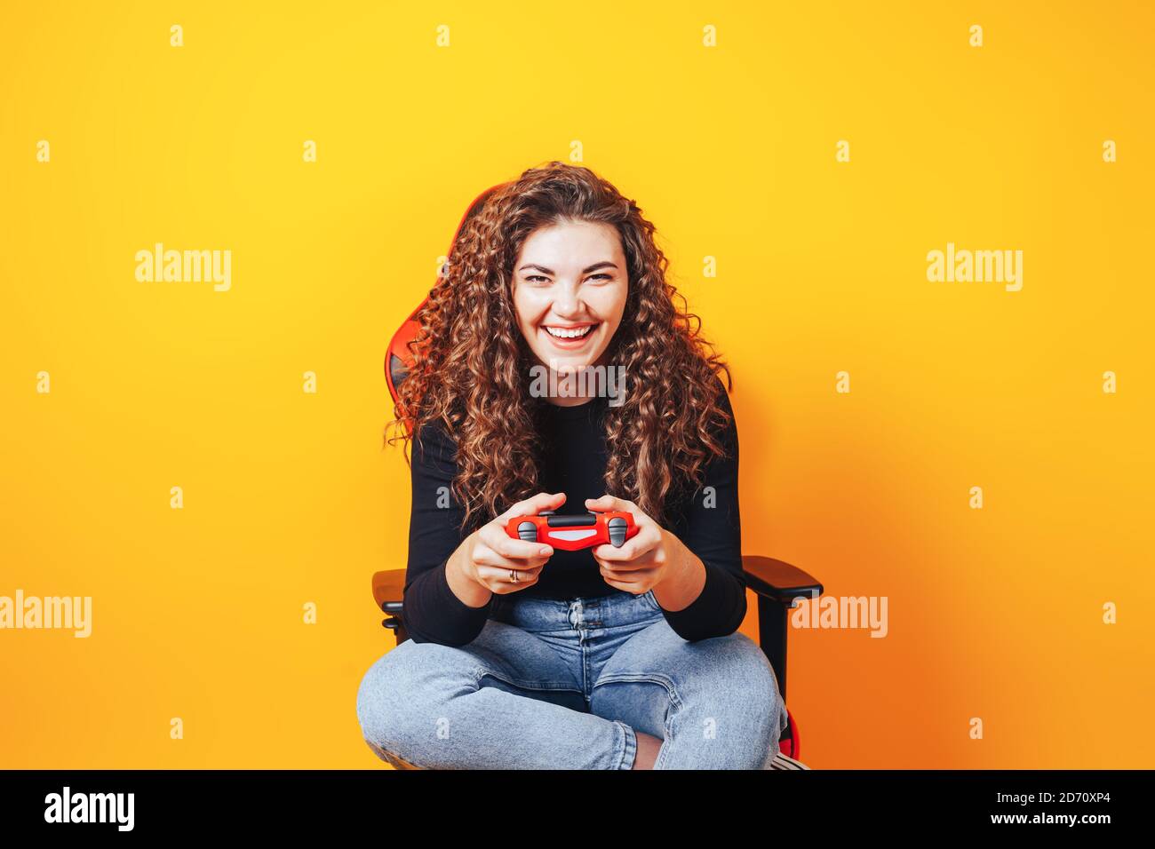 Frau, die hinter einem Spielstuhl in ihren Händen sitzt und rot hält Gamepad auf gelbem Hintergrund Stockfoto
