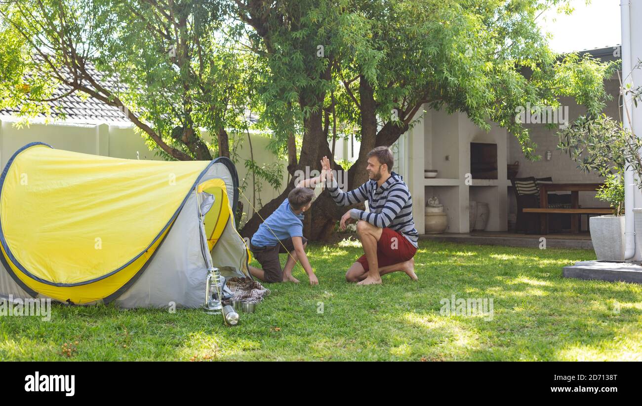 Kaukasischer Mann verbringt Zeit mit seinem Sohn zusammen, Camping im Garten, sitzen am Zelt, hohe Fiving. Soziale Distanzierung während Covid 19 Coronavirus quar Stockfoto