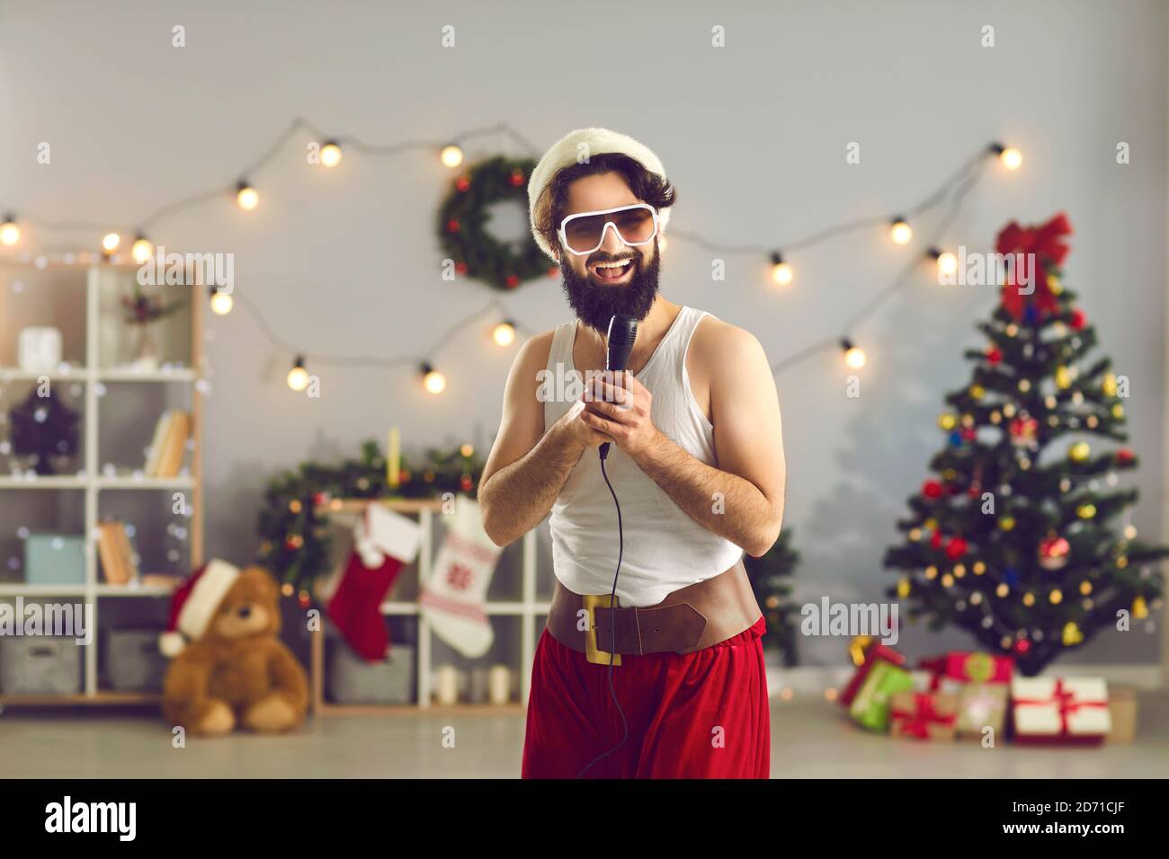 Mann in Weihnachtsmütze und lustige Urlaubskostüm stehen und Singen im Mikrofon Stockfoto