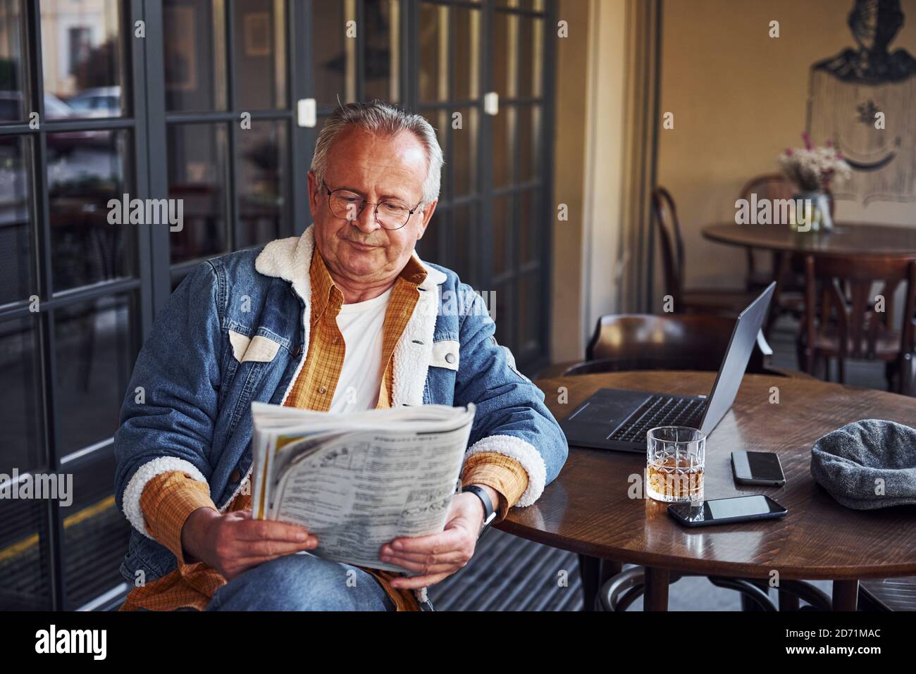 Stilvoller Senior in modischer Kleidung und Brille sitzt in Das Café und liest Zeitung Stockfoto