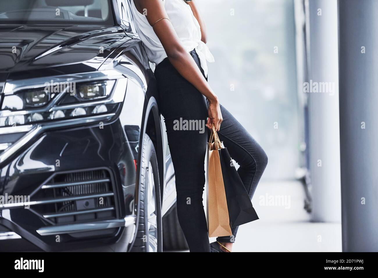 Teilchenansicht der jungen afroamerikanischen Frau in der Brille steht Im Autosalon neben dem Fahrzeug mit Paket in den Händen Stockfoto