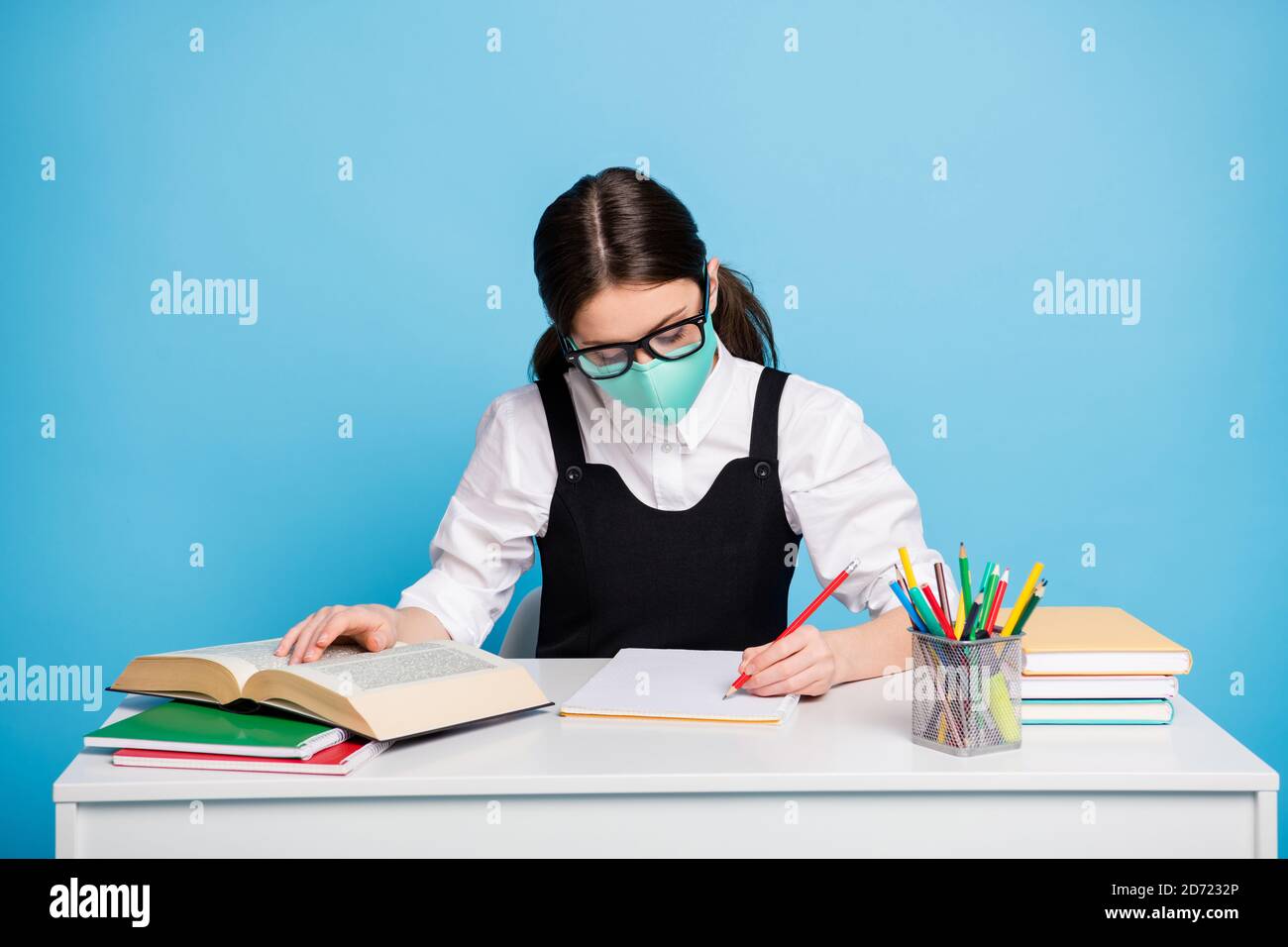 Foto von konzentrierten High School Mädchen sitzen Tisch bereiten Absolvent Prüfung Studie covid Remote schreiben Notiz Buch tragen medizinische Maske Weiße Bluse schwarz Overall Stockfoto