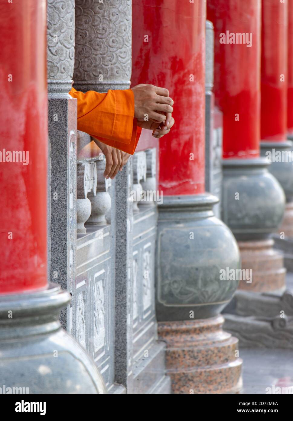 Säulenreihe in einem buddhistischen Tempel mit den Händen eines Mönchs, der auf einem Geländer ruht, Thailand. Stockfoto