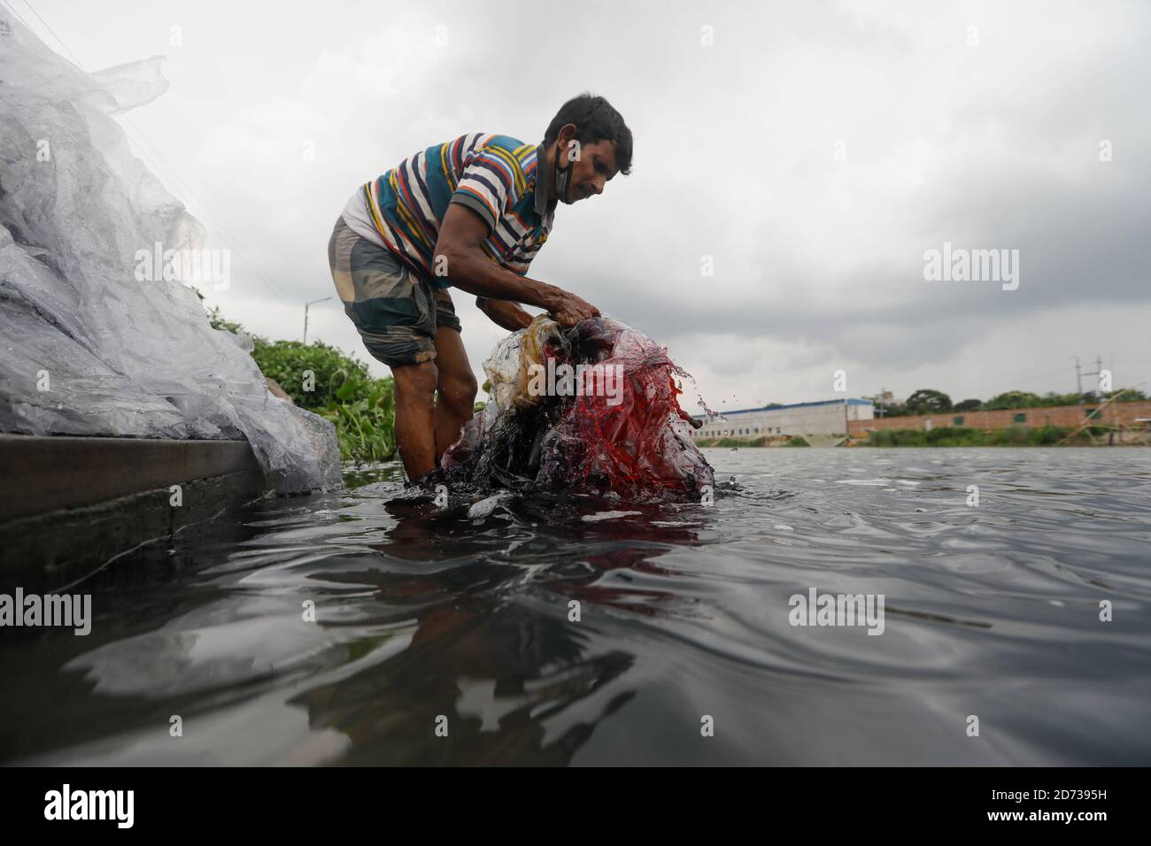 Ein Mann aus Bangladesch wäscht Plastikmüll, der zum Transport von Chemikalien verwendet wurde, im Wasser des Turag-Flusses, bevor er ihn recycelt, in Tongi, in der Nähe von Dhaka, Stockfoto