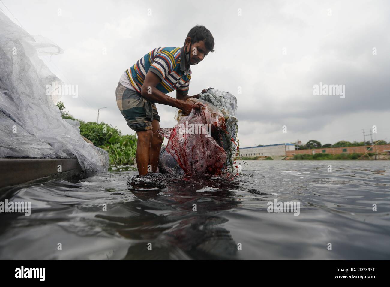 Ein Mann aus Bangladesch wäscht Plastikmüll, der zum Transport von Chemikalien verwendet wurde, im Wasser des Turag-Flusses, bevor er ihn recycelt, in Tongi, in der Nähe von Dhaka, Stockfoto