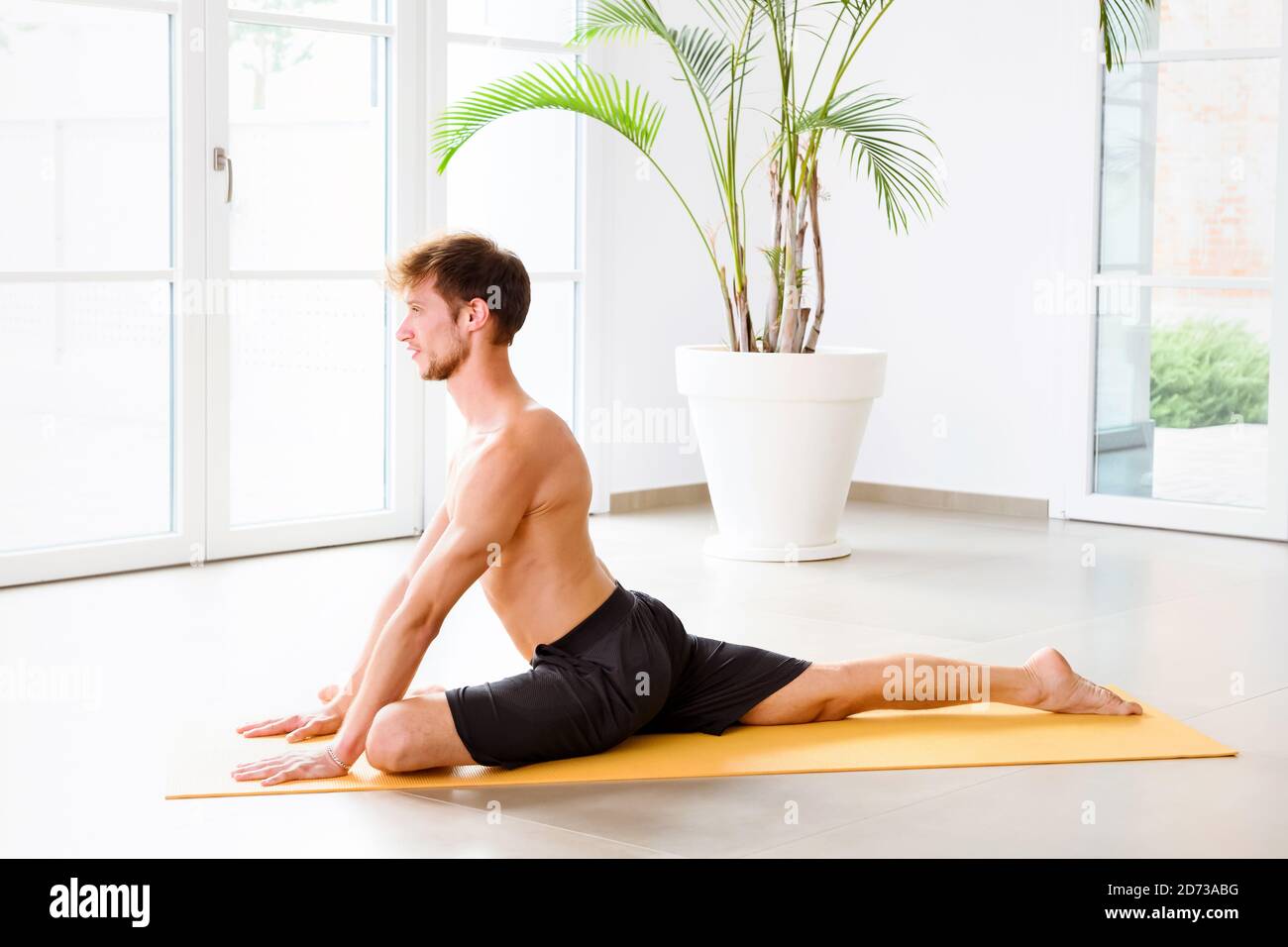 Rajakapotasana oder ein beinigen König Taube Yoga Pose durchgeführt werden Durch einen muskulösen jungen Mann in einem hohen Schlüssel Turnhalle mit Copyspace in einer Gesundheit und fitnes Stockfoto