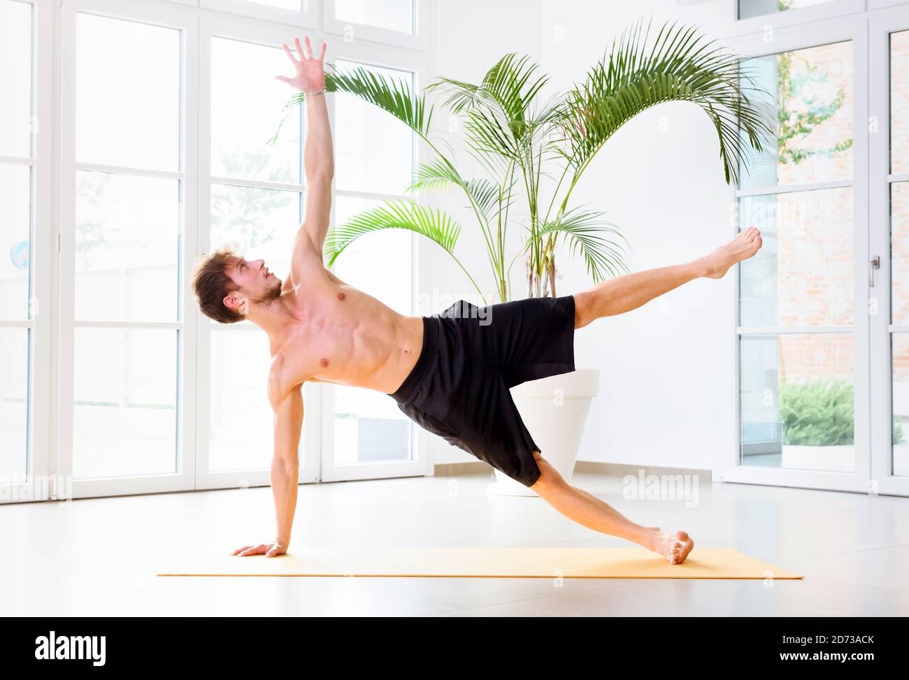 Mann, der eine seitliche Plank Yoga-Übung macht, um seine Kernmuskeln, Arm und Handgelenk in der Seitenansicht in einem High-Key-Fitnessstudio in einem Gesundheits- und Fitnesskonzept zu stärken Stockfoto