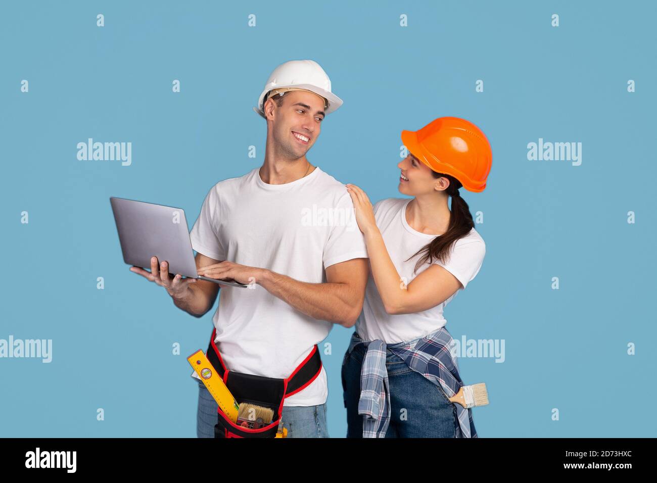 Fröhliches Paar in Hardhats posiert mit Laptop-Computer auf blau studio-Hintergrund Stockfoto