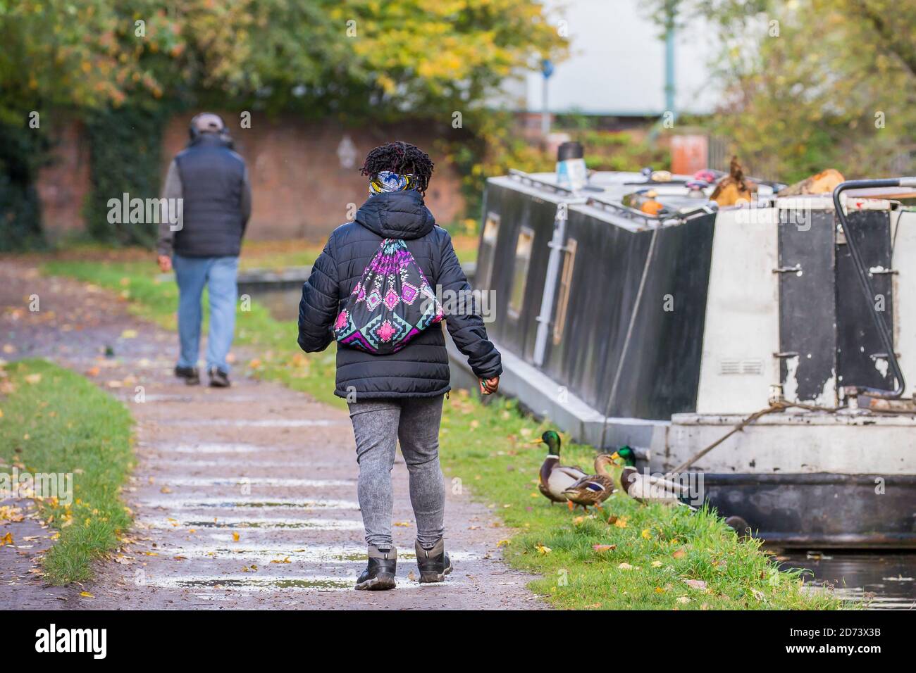 Rückansicht von Fußgängern, die entlang des britischen Kanals towpath, vorbei an einem festfahrenden Schmalboot, Kanalboot, im Herbst gehen. Stockfoto