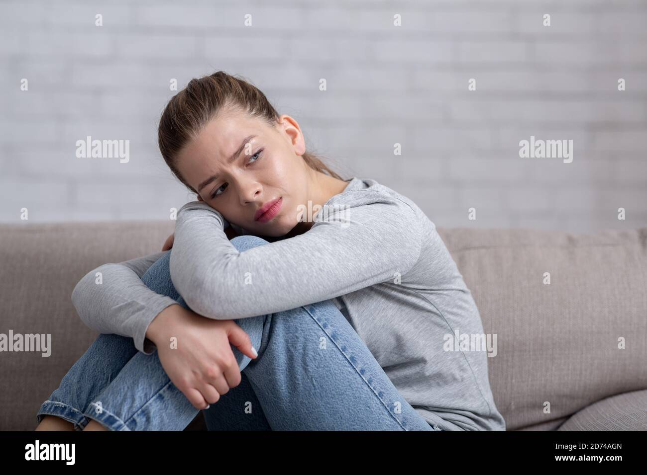 Depression und Angst Konzept. Junge traurige Frau, die auf dem Sofa sitzt und ihre Knie umarmt, Platz kopieren Stockfoto