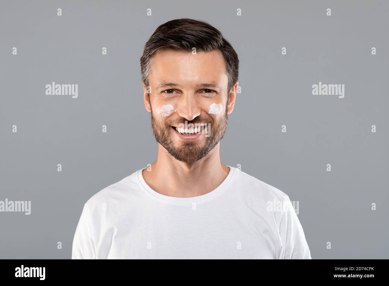 Mann mittleren Alters mit Creme auf den Wangen gegen Falten Stockfoto
