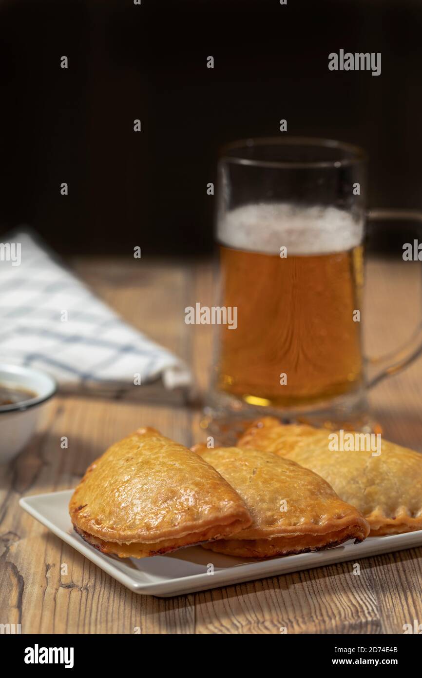 Argentinier Fleisch Empanadas mit einem Glas Bier über ein Holztisch Stockfoto