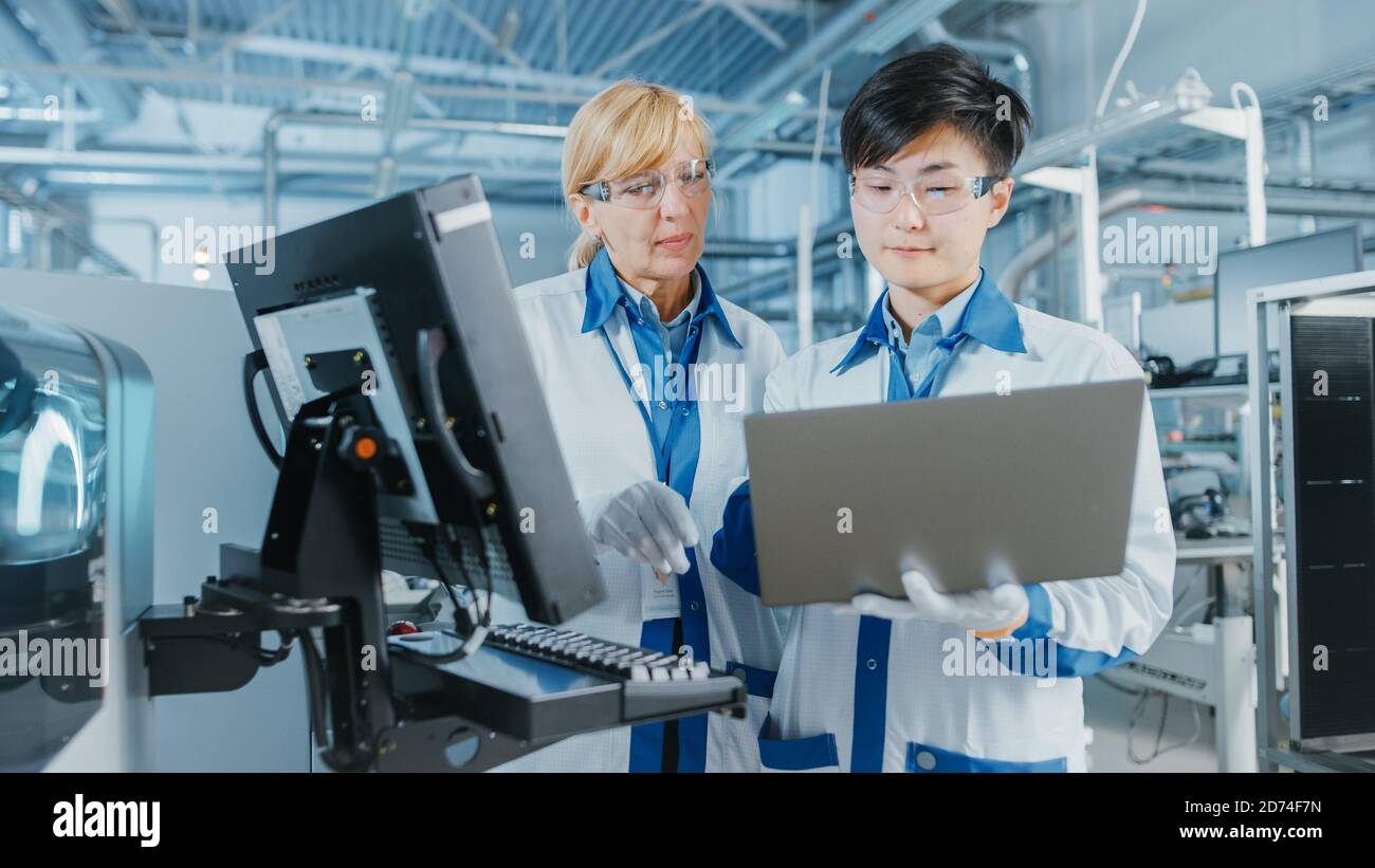 Auf High-Tech-Fabrik Asian Engineer Gespräche mit weiblichen Vorgesetzten, verwenden Sie Computer für die Programmierung Pick-and-Place elektronische Maschinen für gedruckte Schaltung Stockfoto