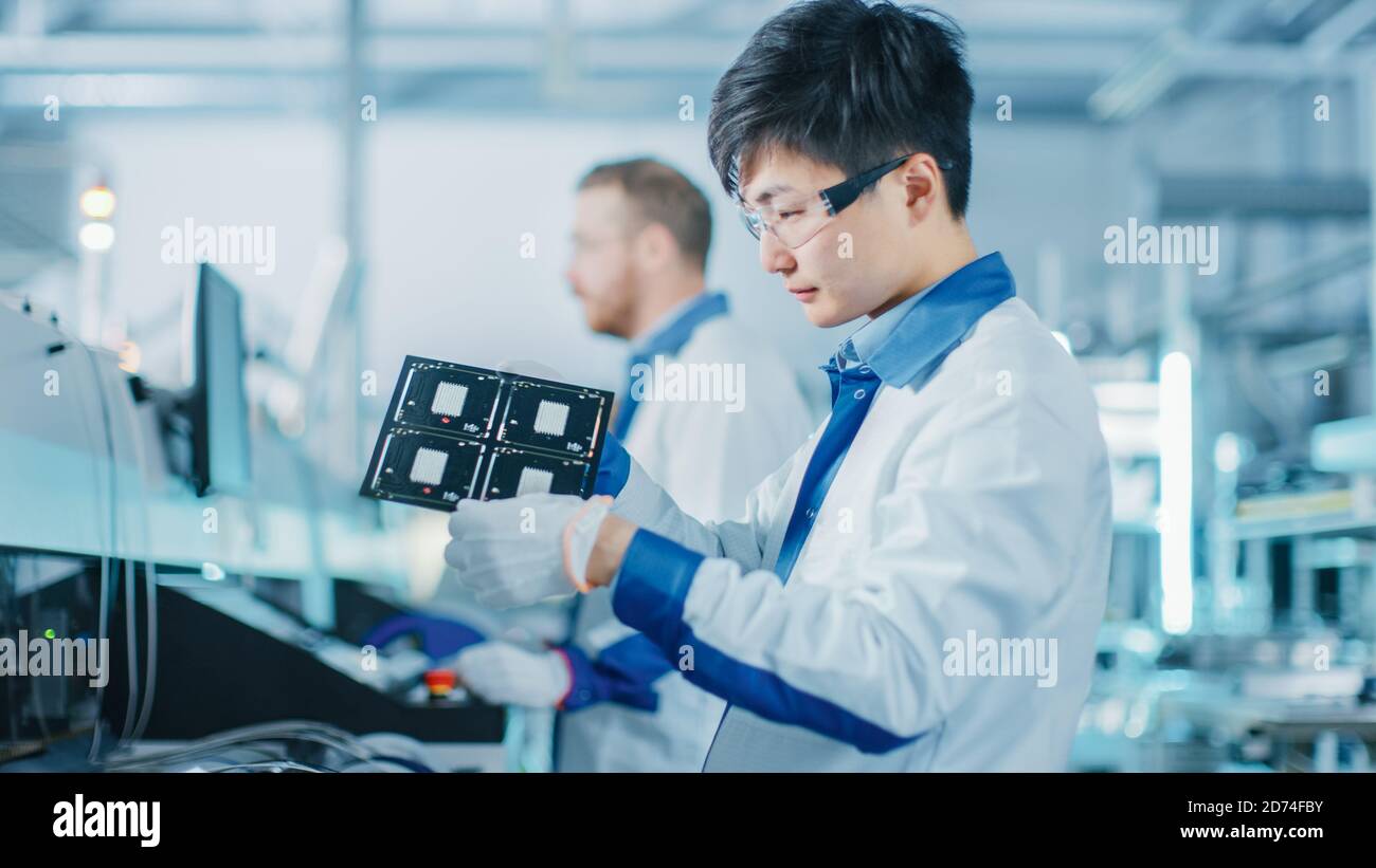 High-Tech Factory: Qualitätsingenieur prüft elektronische Leiterplatten-IT auf Schäden. In der Background Assembly Line für Leiterplatte mit Stockfoto