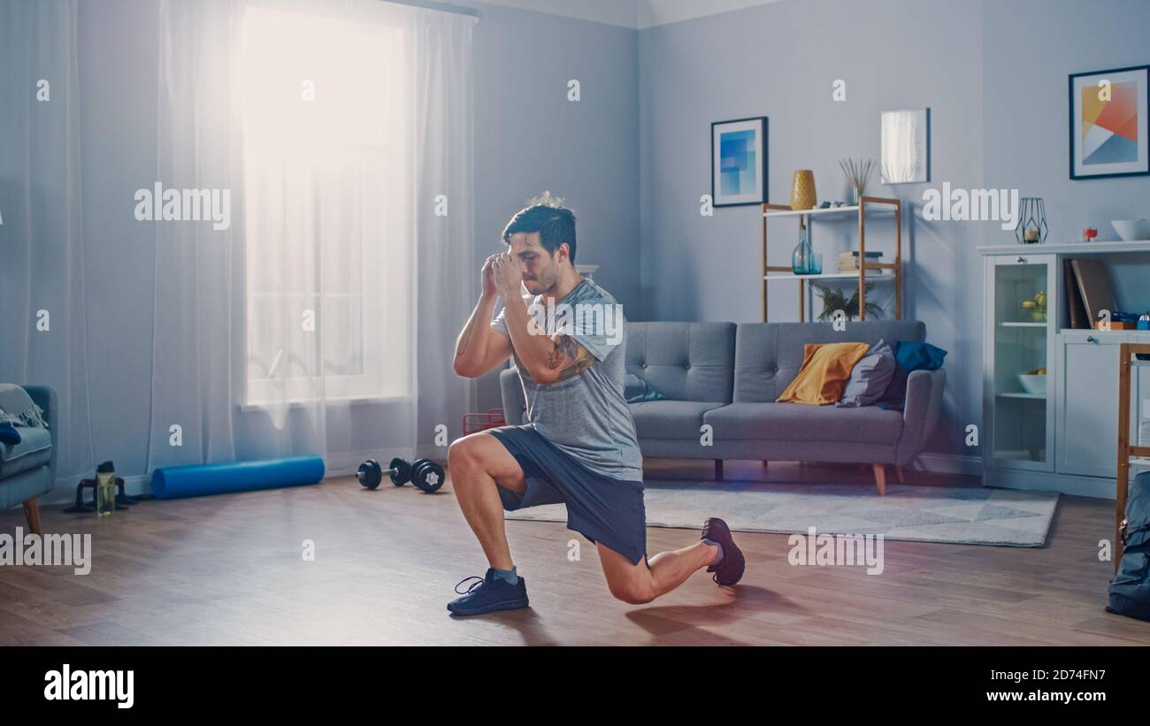 Starke Athletic Fit Mann in T-Shirt und Shorts tut Vorwärts Ausfallschritt Übungen zu Hause in seiner geräumigen und hellen Wohnung mit minimalistischem Interieur Stockfoto